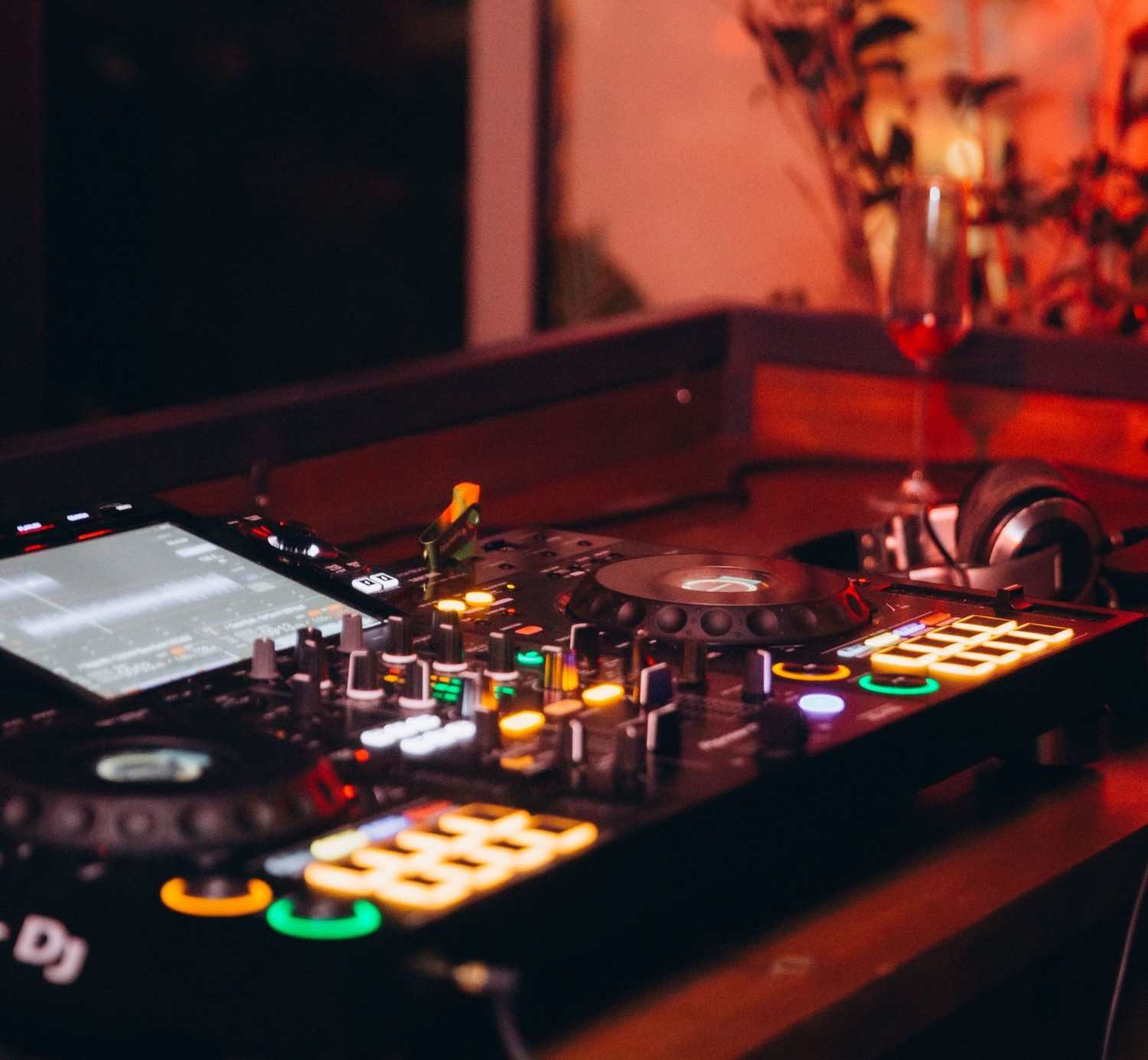 Colorful DJ mixer and headphones on a wooden table in a dimly lit nightclub, exuding a lively atmosphere.